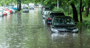Cars parked along a street are submerged in deep flood water.